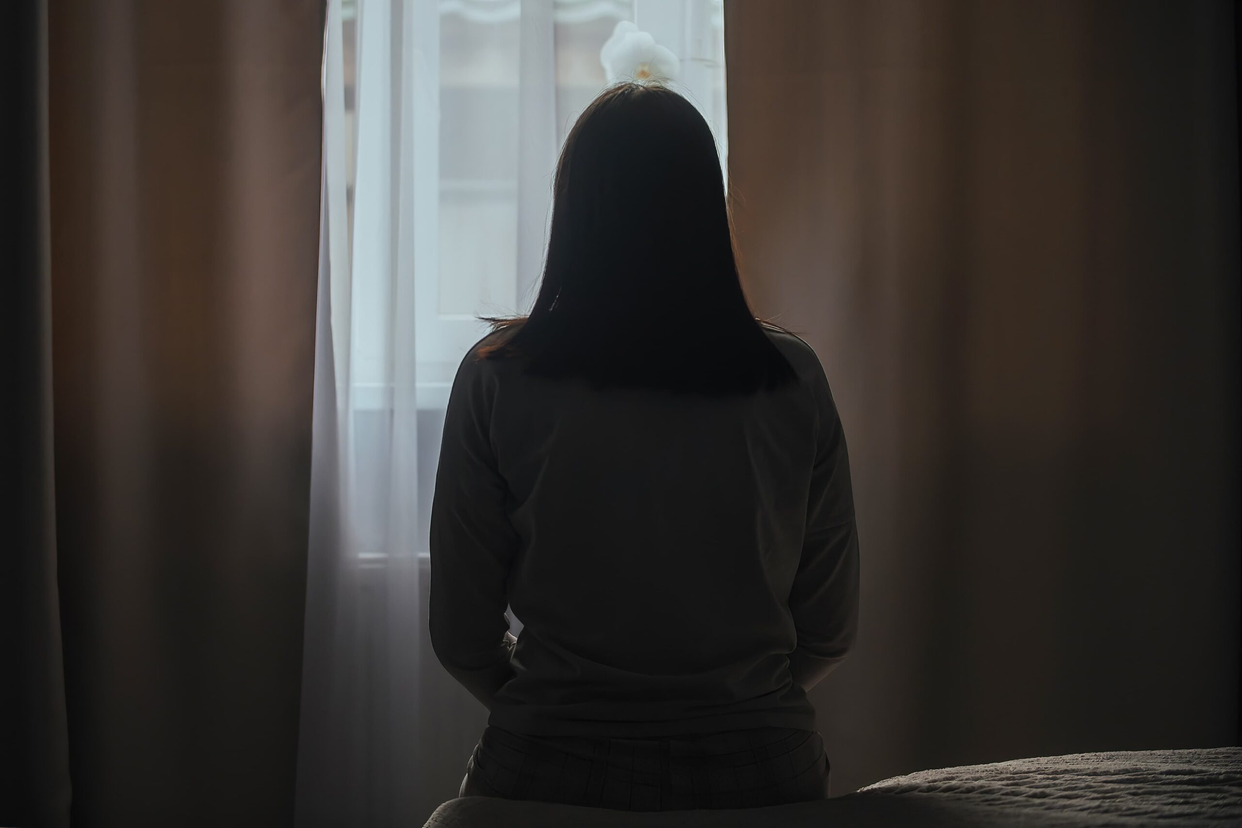 Silhouette of a woman sitting in her bed looking out her window